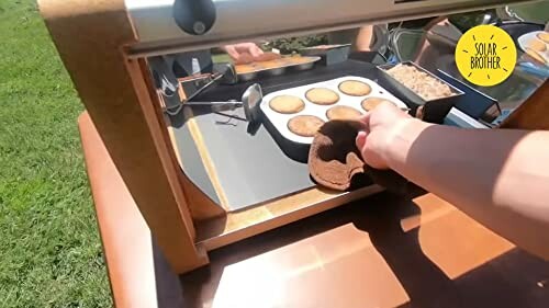 Hand nimmt Gebäck aus Solarkocher.